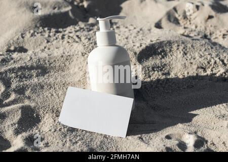 Cartoleria estiva scena ancora di vita. Idratante cosmetico, crema o bottiglia di shampoo nella sabbia da spiaggia. Carta bianca, scena di mockup di invito Foto Stock