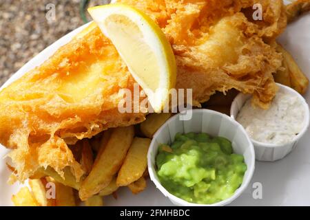 Pesce e patatine, con lato di piselli e salsa tartare, serviti all'aperto in un pub Suffolk, East Anglia, Regno Unito Foto Stock