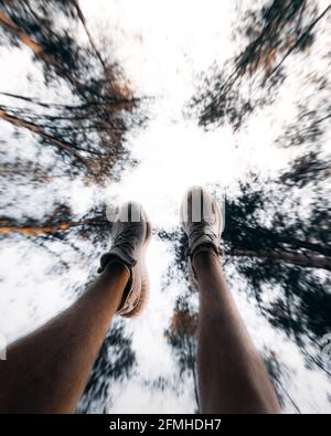 Un'angolazione ridotta dei piedi di una persona nel aria in una foresta sotto la luce del sole con un offuscato sfondo Foto Stock