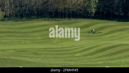 Un singolo golfista cammina attraverso un prato a strisce sul campo da golf dell'Hollins Hall Hotel a Baildon, Yorkshire, Inghilterra. Foto Stock