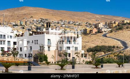 La città collinare di Wadi Musa, Giordania, con bassi edifici residenziali e alberghieri e strada sotto il cielo azzurro in una giornata estiva Foto Stock