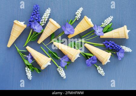 Delizioso dessert in coni di waffle su sfondo blu con fiori di primavera. Vista dall'alto Foto Stock