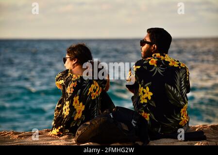 Coppia sposata che guarda il tramonto, indossando camicie Hawaiiane abbinate con stampe floreali, Sunset Beach, Haleiwa, Hawaii, USA Foto Stock