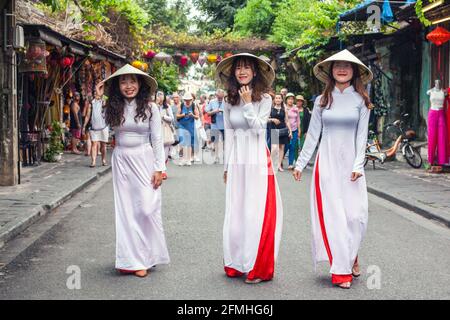 Tre donne vietnamite vestite con cappelli conici e abiti tradizionali di ao dai, Hoi An, Vietnam Foto Stock