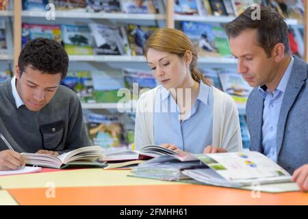 tre persone si sedettero attorno al tavolo studiando Foto Stock