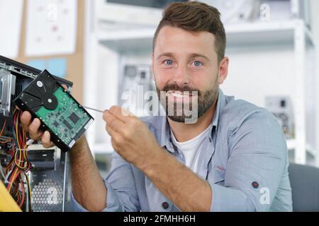 uomo che inripara un computer portatile utilizzando un cacciavite Foto Stock