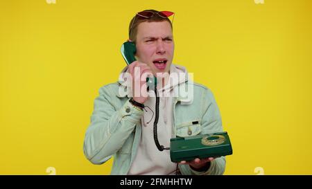 Uomo teen sincero pazzo che parla su telefono vintage cablato degli anni '80, imbrogliando, rendendo stupido facce divertenti Foto Stock