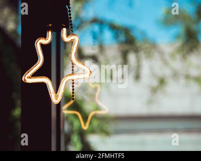 Decorazioni a forma di stella con lampadine al caffè. Lampada a LED in stile retrò che risplende vicino alla finestra in vetro con spazio per la copia. Foto Stock