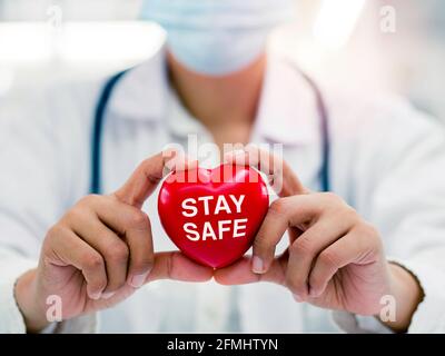 Concetto di sicurezza, assistenza sanitaria e medicina. Primo piano delle mani del medico femminile che tiene il cuore rosso con la parola soggiorno sicuro, Campagna per le persone a rimanere hom Foto Stock