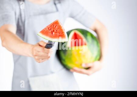 Una giovane donna caucasica sta tagliando un cuneo da un cocomero maturo usando un coltello. Il melone è maturo con la macchia di campo. Frutta di stagione estiva leggera e ariosa c Foto Stock
