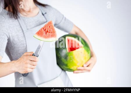 Una giovane donna caucasica sta tagliando un cuneo da un cocomero maturo usando un coltello. Il melone è maturo con la macchia di campo. Frutta di stagione estiva leggera e ariosa c Foto Stock