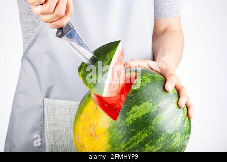 Una giovane donna caucasica sta tagliando un cuneo da un cocomero maturo usando un coltello. Il melone è maturo con la macchia di campo. Frutta di stagione estiva leggera e ariosa c Foto Stock