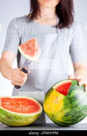 Una giovane donna caucasica sta tagliando un cuneo da un cocomero maturo usando un coltello. Il melone è maturo con la macchia di campo. Frutta di stagione estiva leggera e ariosa c Foto Stock