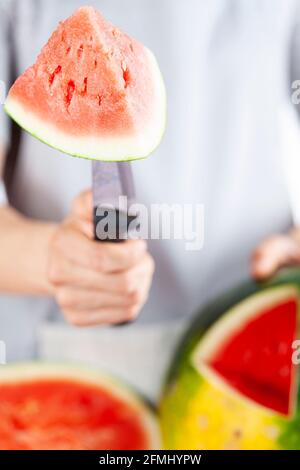 Una giovane donna caucasica sta tagliando un cuneo da un cocomero maturo usando un coltello. Il melone è maturo con la macchia di campo. Frutta di stagione estiva leggera e ariosa c Foto Stock