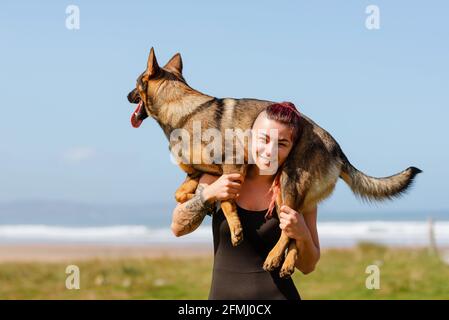 Atleta femmina tatuata con carino cane purebred sulle spalle guardando a macchina fotografica il giorno di sole Foto Stock