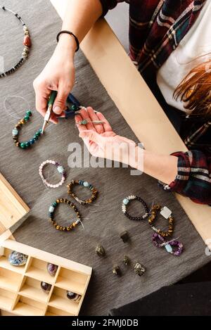 Dall'alto, una donna non riconoscibile, seduta al tavolo camion e creare braccialetti fatti a mano durante il viaggio Foto Stock