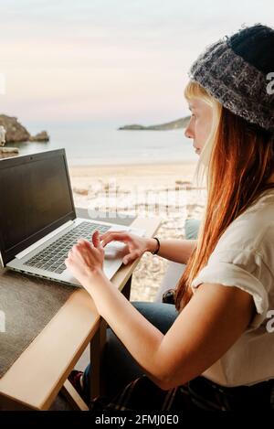 Vista laterale di una donna che viaggia libera e che si siede in parcheggio camion con computer portatile che lavora su progetti remoti Foto Stock