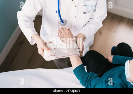 Alto angolo di raccolto anonimo medico in garza uniforme di imballaggio intorno al polso del paziente in ospedale Foto Stock