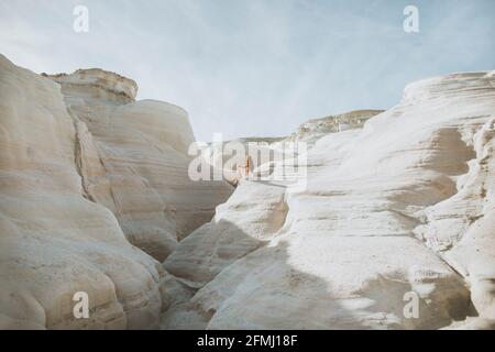 Indietro vista anonima femmina in bianco Sundress passeggiando lungo stretto passaggio formato da rocce curvy chiaro su tempo soleggiato in Sarakiniko Grecia Foto Stock
