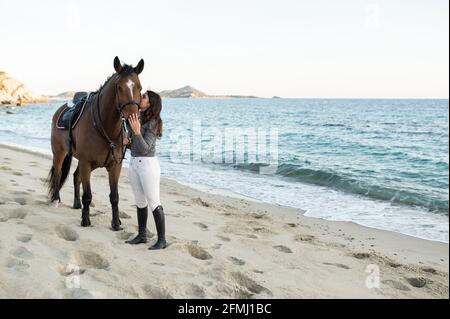 Giovane femmina baciante muso di stallone di castagno in briglia contro oceano ondulato Foto Stock