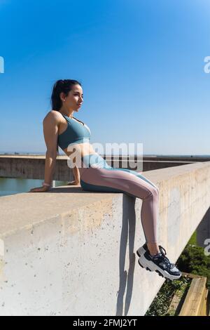 Vista laterale dell'atleta in vestiario sportivo lontano da recinto di cemento sotto il cielo blu Foto Stock