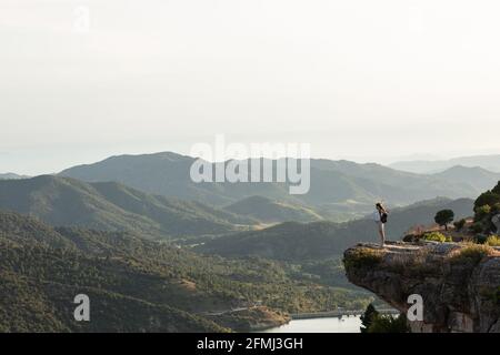 Vista remota di un'escursionista femminile in piedi con le braccia aperte bordo di collina e godendo la libertà durante il trekking in montagna in estate Foto Stock
