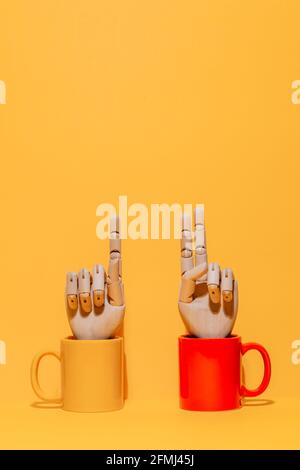 Mano di legno ornamentale creativa con indice e dito medio insieme gesto  all'interno della tazza colorata su sfondo giallo e rosso studio Foto stock  - Alamy