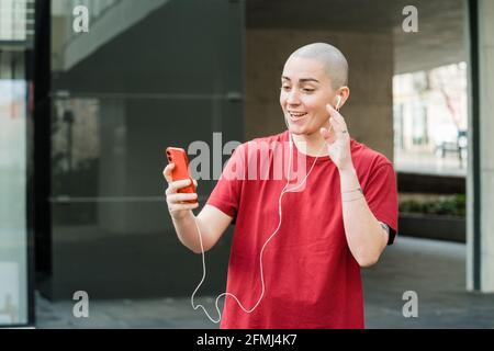 Persona transgender negli auricolari che svela la mano durante la chat video su telefono cellulare contro l'edificio in città Foto Stock