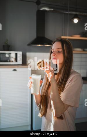 Giovane donna allegra con gustoso biscotto di farinata d'avena con patatine al cioccolato per la colazione sul tavolo in cucina Foto Stock