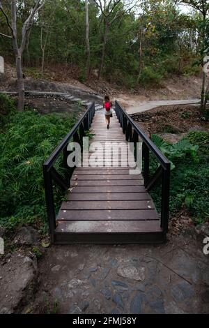 Vista laterale di African American femmina con lunghe trecce in elegante vestito in piedi e sollevamento felice figlia mentre si diverte in strada in soleggiato Foto Stock