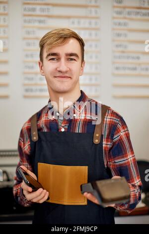 barista in grembiule tenere moderno terminale di pagamento bancario Foto Stock