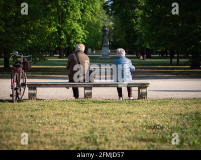 Un uomo anziano e una donna che siedono lontano su un banco in un parco pubblico. Foto Stock