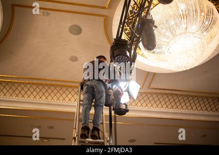 Il tecnico di luce maschile sta organizzando le luci di fase di fissaggio su tralicci per le prove di esposizione. Impostazione del sistema di illuminazione del palco. Foto Stock