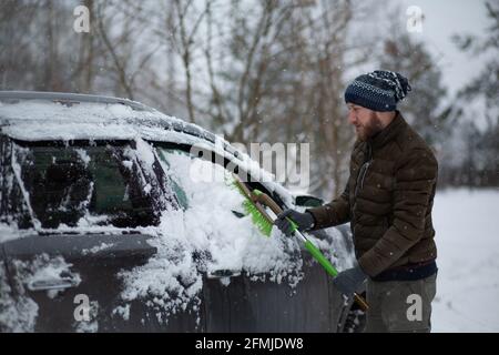 Uomo che pulisce la sua auto dalla neve con una spazzola in una giornata invernale. Foto Stock