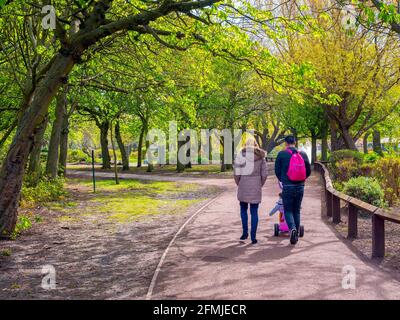 Una soleggiata giornata di primavera a Locke Park Lake Redcar North Yorkshire con foglie fresche sugli alberi di salice e un coppia che spinge un bambino in buggy Foto Stock