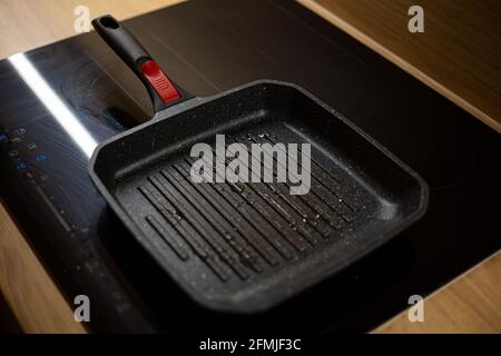 La teglia nera per grigliate oleosa si sta riscaldando su un piano cottura elettrico in ceramica per la cottura degli hamburger a casa. Foto Stock