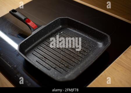 La teglia nera per grigliate oleosa si sta riscaldando su un piano cottura elettrico in ceramica per la cottura degli hamburger a casa. Foto Stock