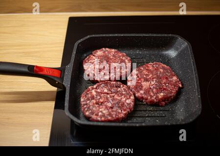 Burger cotoletta di carne di manzo sminuzzata cruda su una padella alla griglia. Processo di cottura self-made hamburger a casa. Foto Stock