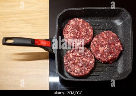 Burger cotoletta di carne di manzo sminuzzata cruda su una padella alla griglia. Processo di cottura self-made hamburger a casa. Foto Stock