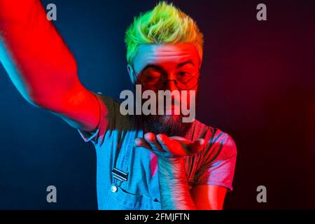 Romantico uomo hipster bearded con barba in tute in denim che parla via web camera con la fidanzata, esprimendo l'amore, trasmettendo in diretta streaming. Colorato Foto Stock