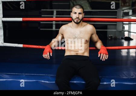 Combattente che pratica alcuni calci con la sacca di punzonatura. Calcio, sacchetto di punzonatura su sfondo scuro. Il sacchetto nero per punzonatura pesa in palestra Foto Stock