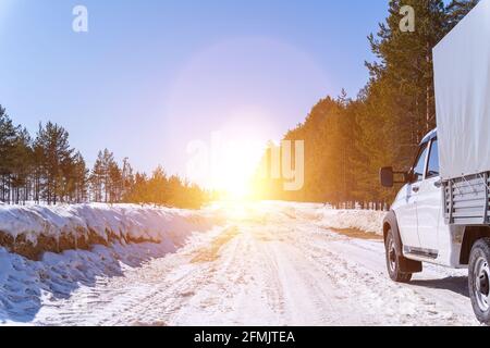 Auto bianca su una strada invernale attraverso una foresta innevata. Vista dal basso. Auto su strada innevata invernale in montagna in giornata di sole. Foto Stock