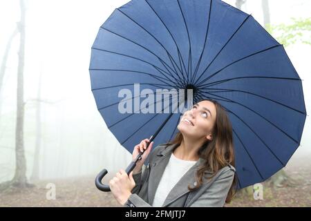 Donna felice sotto ombrello guardando la pioggia che cammina dentro un parco di nebbia Foto Stock