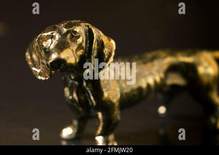 Un macro primo piano di un Dachshund lungo cane bronzo figura modello su sfondo scuro. Messa a fuoco selettiva estrema. Foto Stock