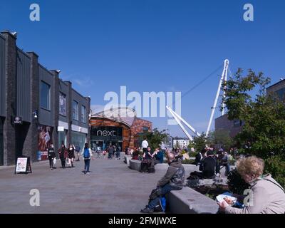 Persone che si siedono al sole nel centro pedonale della città con Usk ponti in background Newport Gwent Galles del Sud Regno Unito Foto Stock