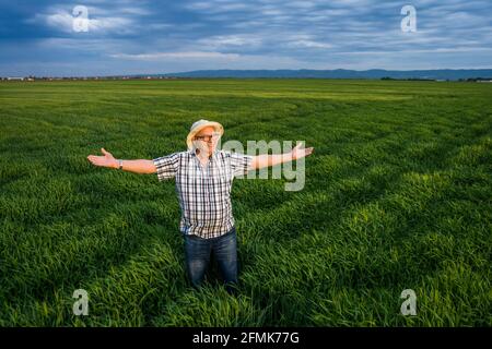Orgoglioso agricoltore anziano è in piedi nel suo campo d'orzo e godendo il tramonto. Foto Stock