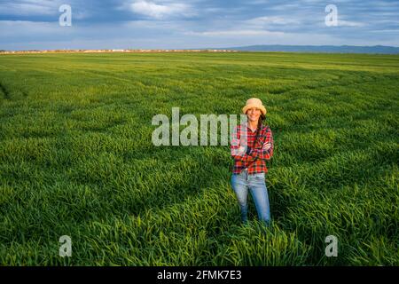Orgogliosa agricoltore femminile è in piedi nel suo campo di orzo e godendo il tramonto. Foto Stock