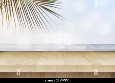 Tavolo in legno su sfondo di spiaggia sfocato con foglia di palma. Summer Concept, montaggio per l'esposizione dei prodotti. Foto Stock