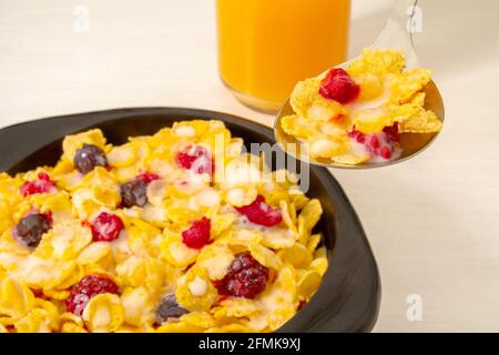 Colazione sana al cornflakes con lampone, mirtillo e latte in ciotola di legno nero e su un cucchiaio per la colazione Foto Stock