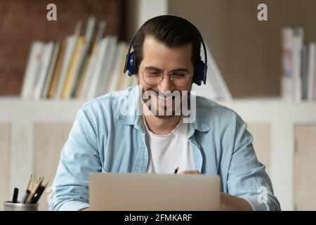 Primo piano uomo sorridente in cuffia guardando lo schermo del computer portatile Foto Stock